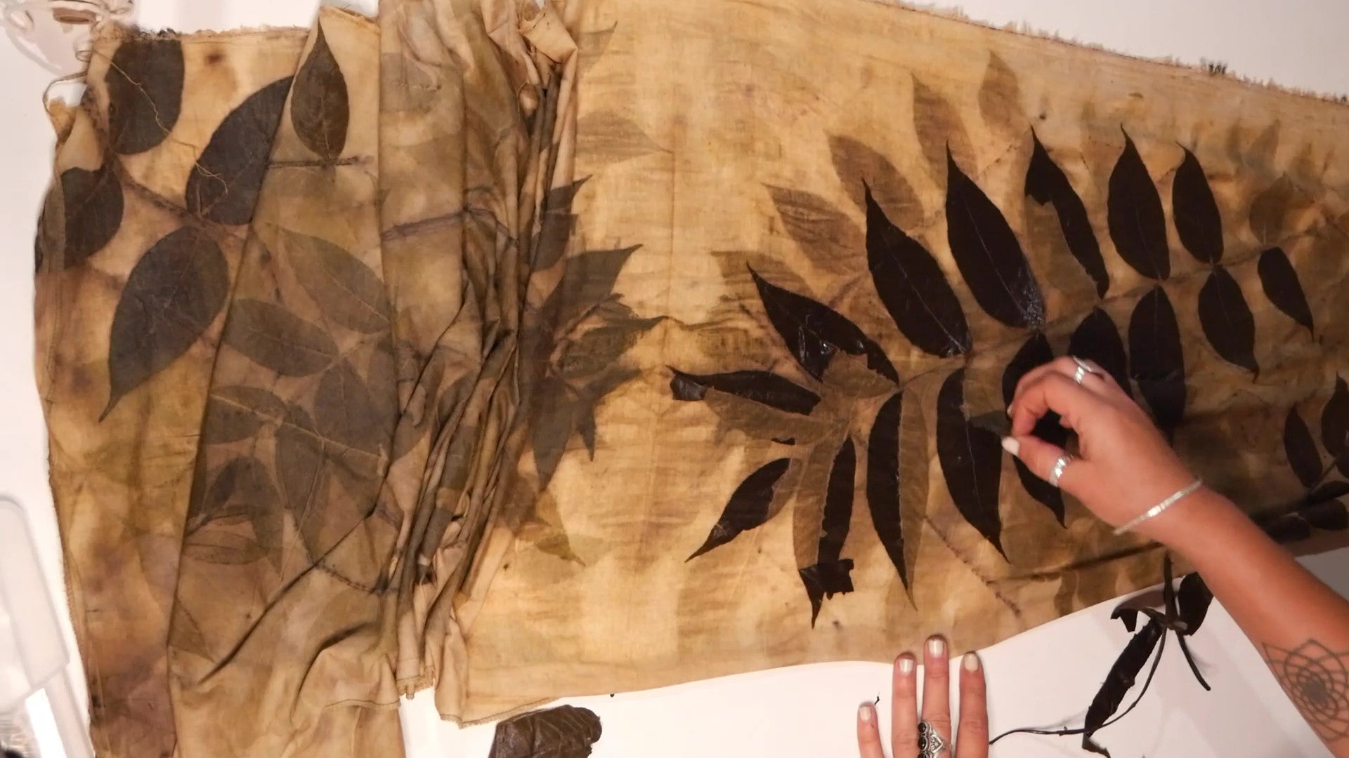 Load video: sped up video showing leaves being pulled off fabric to reveal permanent  print.