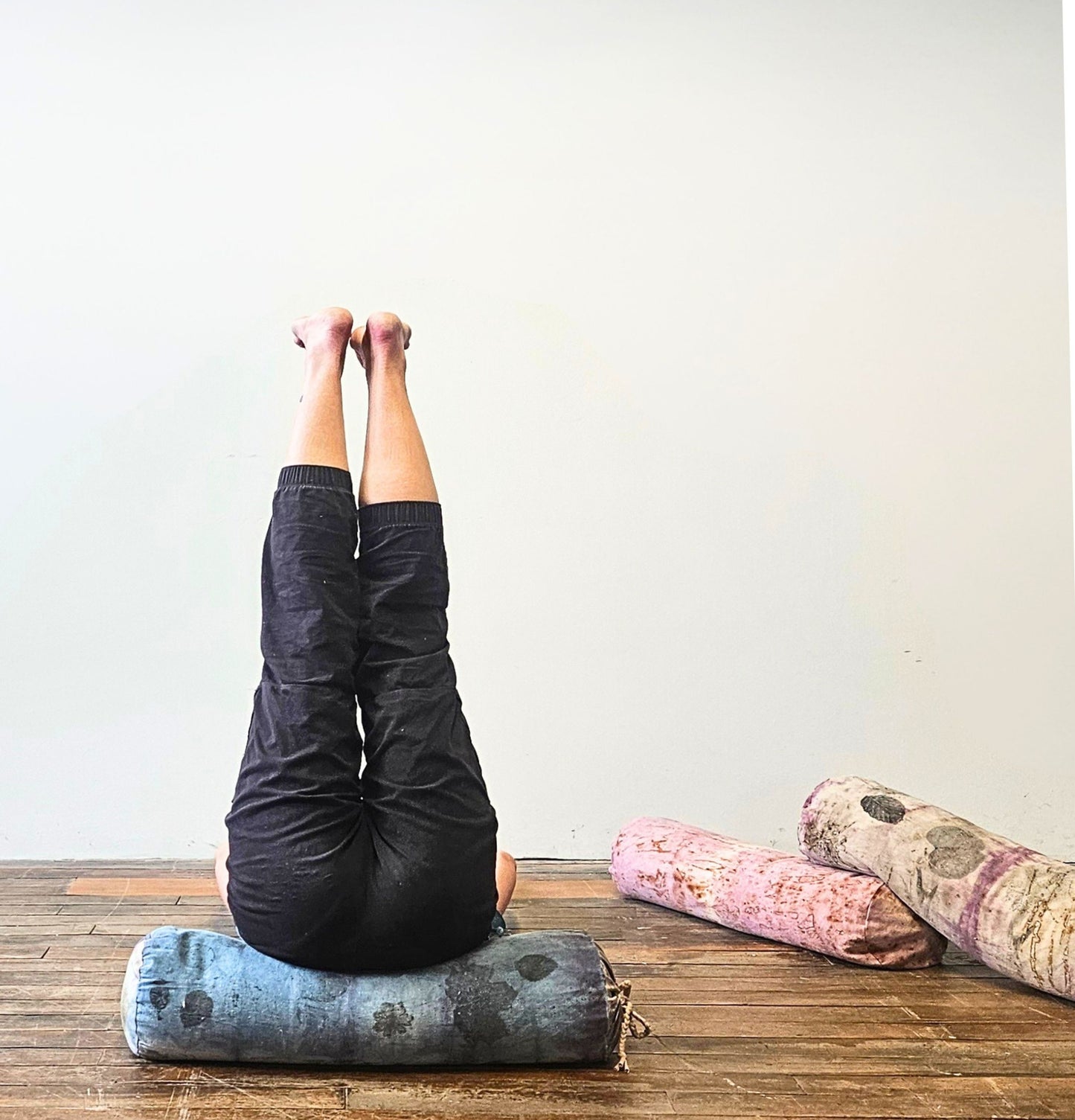 Person practicing yoga with bolsters on a wooden floor against a white wall